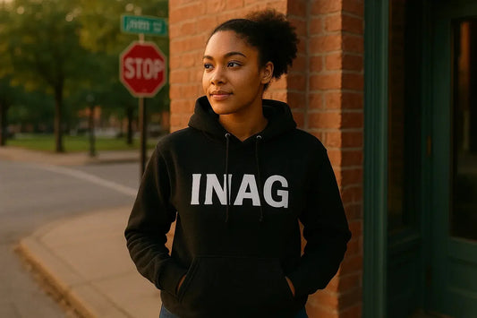 Man wearing a black INAG purpose-driven streetwear hoodie, standing confidently beside a brick building.